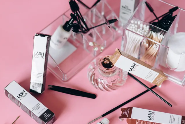 Flat lay of various cosmetic tools and products on a pink surface with clear organizers. Assortimento e prodotti principali