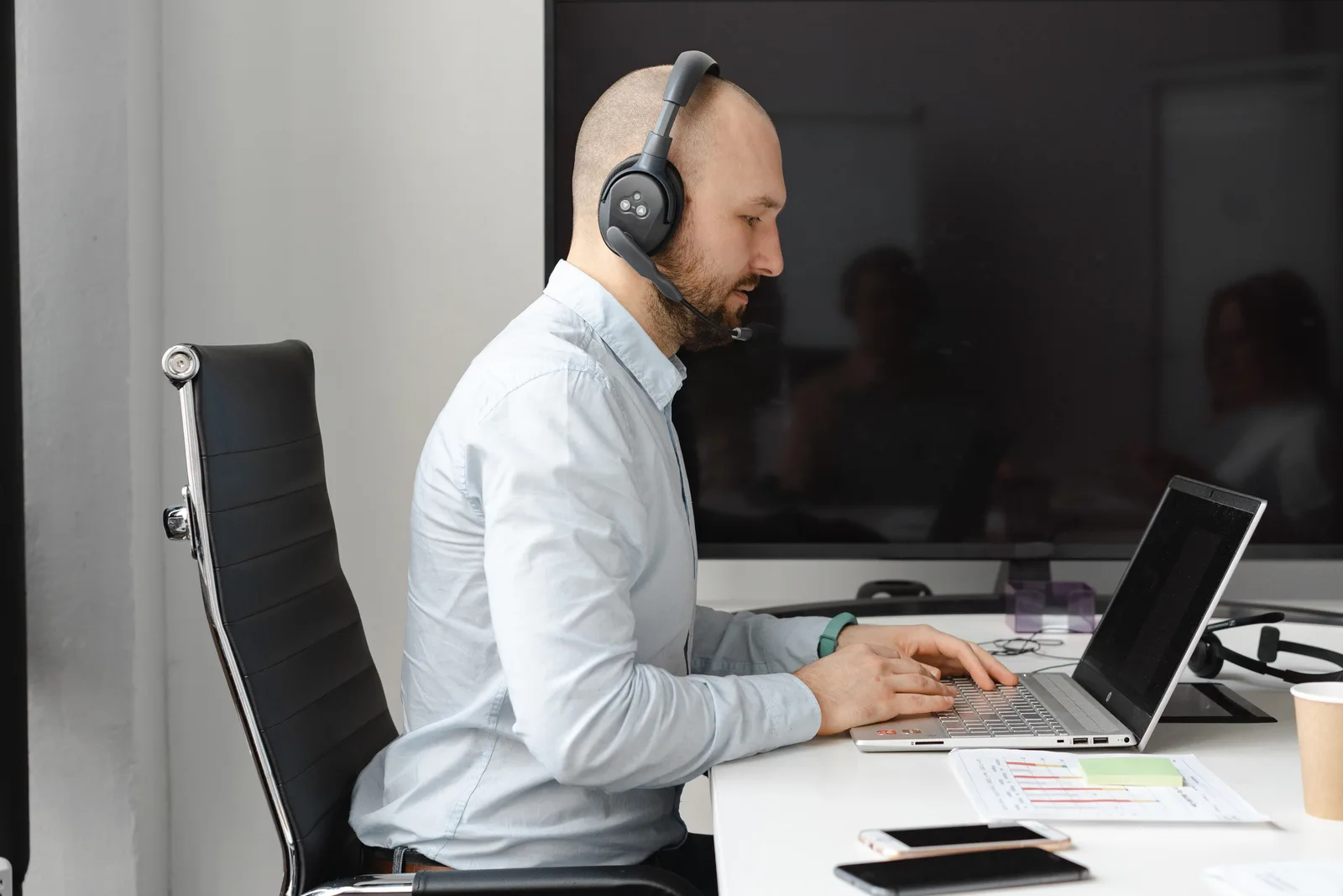 A focused call center agent with headphones working on a laptop in an office.