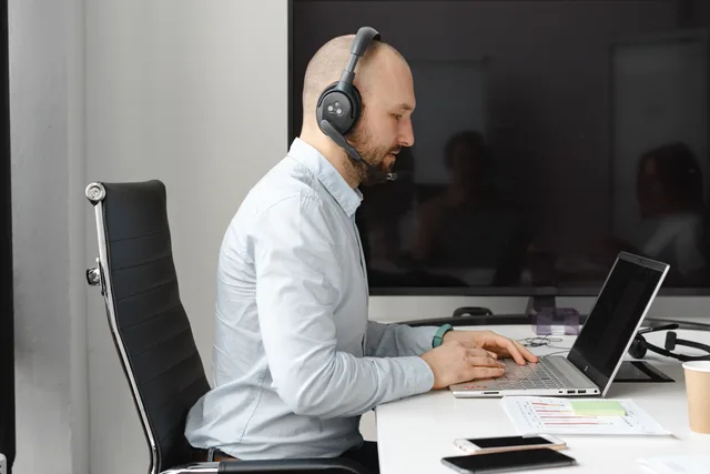 A focused call center agent with headphones working on a laptop in an office. Chiedere riscontri dopo l'uso del prodotto: quando e come