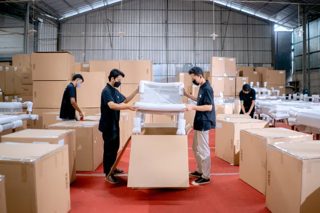 Men in a warehouse wearing masks, assembling and packing furniture into boxes with efficiency. Confrontare gestione interna e partner logistico: costi