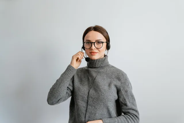 Caucasian woman in gray sweater and glasses providing customer support using a headset in an office. Informare i clienti di una modifica realmente introdotta