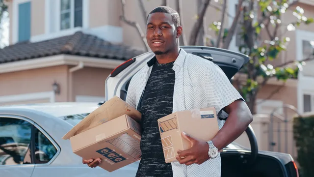 A courier in a residential area delivering packages from a car trunk, representing efficient delivery service. Logistica per un piccolo brand