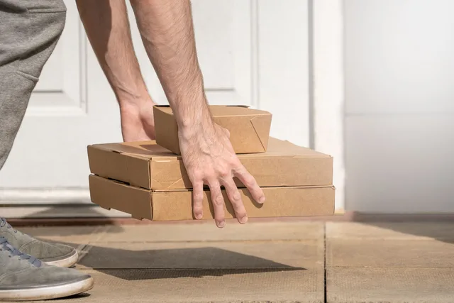 A photo of a delivery driver carefully placing three takeaway boxes on the floor in front of a white door. The boxes are made of cardboard. This image is free to use under Creative Commons. If you end up using it, please throw in a link to our website at meanwell-packaging.co.uk/. Valutare un fornitore dal servizio promesso ai clienti